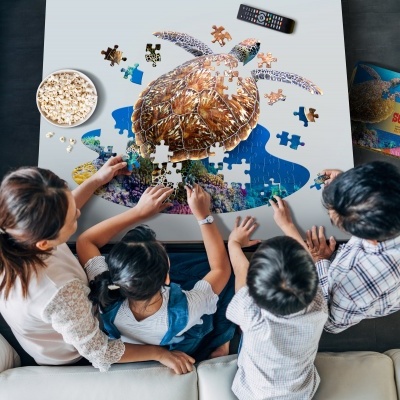 Quatro pessoas montam puzzle de tartaruga marinha numa mesa branca com pipocas e caixa do puzzle.