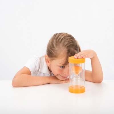 Menina loira a olhar para um ampulheta amarelo transparente numa mesa branca