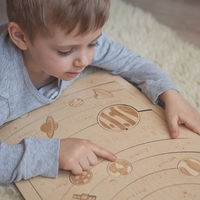 Criança com painel didático do sistema solar em tons castanhos