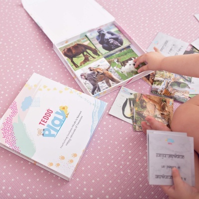 Jogo de cartas infantil com imagens de animais sobre superfície rosa e mãos de criança a mexer nas cartas