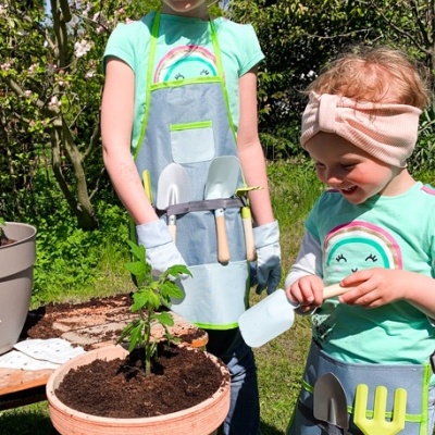 Duas crianças com aventais e ferramentas de jardinagem em ambiente ao ar livre