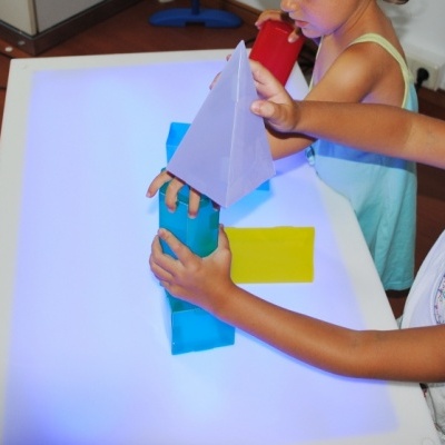 Crianças a brincar com blocos de construção coloridos sobre superfície branca iluminada