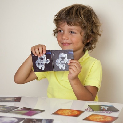 Menino segurando cartas com imagens de astronautas sentado à mesa com outras cartas espalhadas