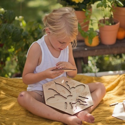 Criança brinca com brinquedo educativo em madeira sentada num tecido amarelo