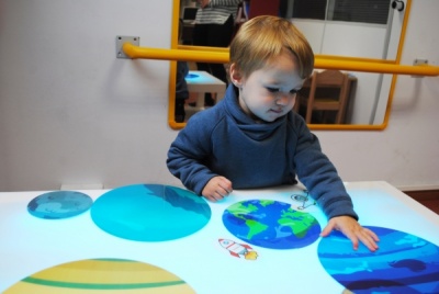 Criança com suéter azul interage com superfície iluminada e círculos coloridos