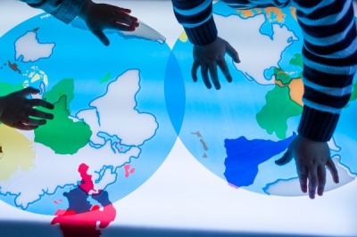 Mapa-múndi colorido iluminado com mãos de crianças a tocar
