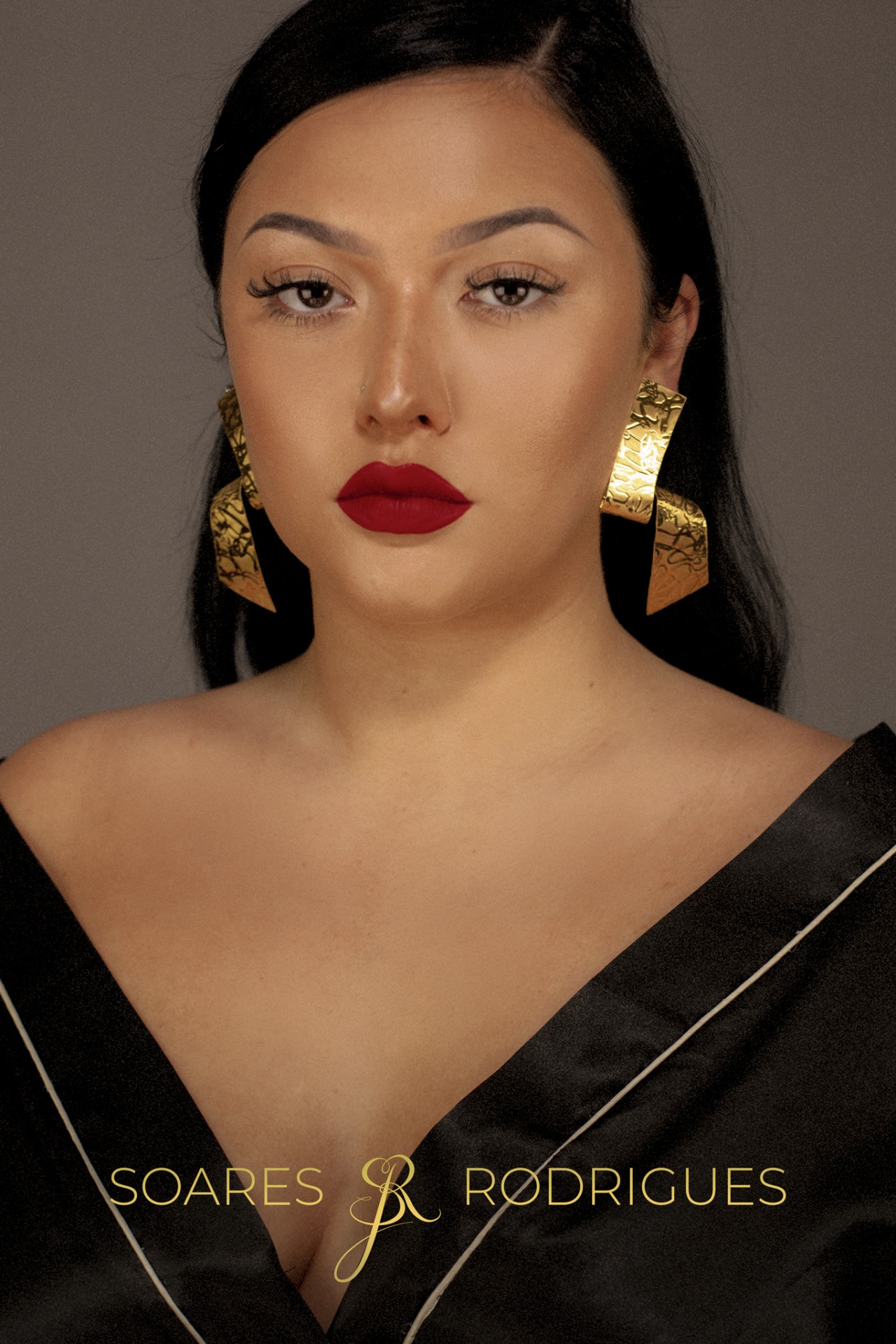 Brincos Samurai Mulher com brincos dourados texturizados e vestido preto com decote profundo