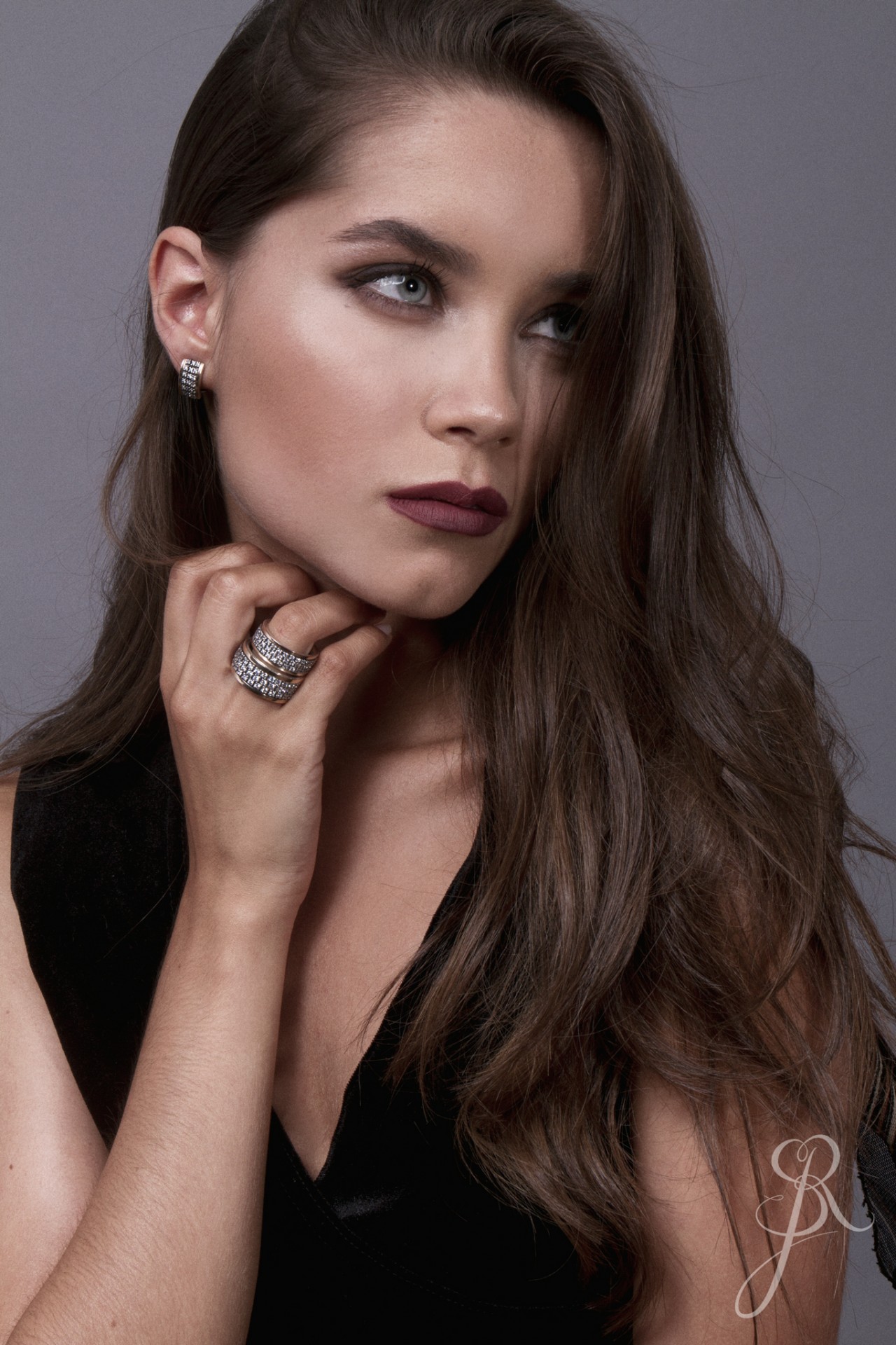 Aliança Rotativa c/Zircónias Mulher com brincos e anéis prateados com pedras brilhantes, roupa preta e fundo cinzento