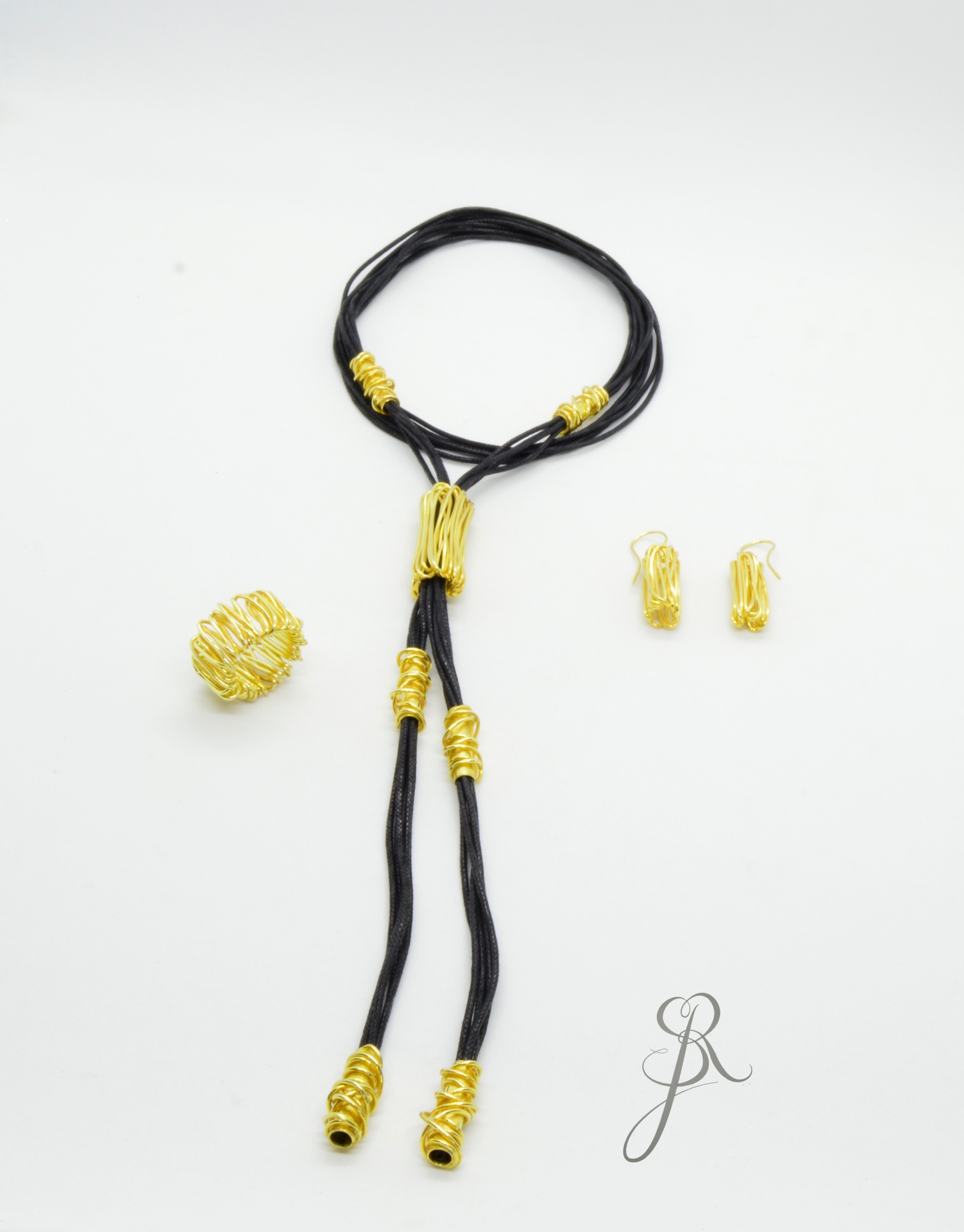 Brincos de Fios Conjunto de bijuteria com colar preto e dourado, anel dourado e brincos dourados sobre fundo branco