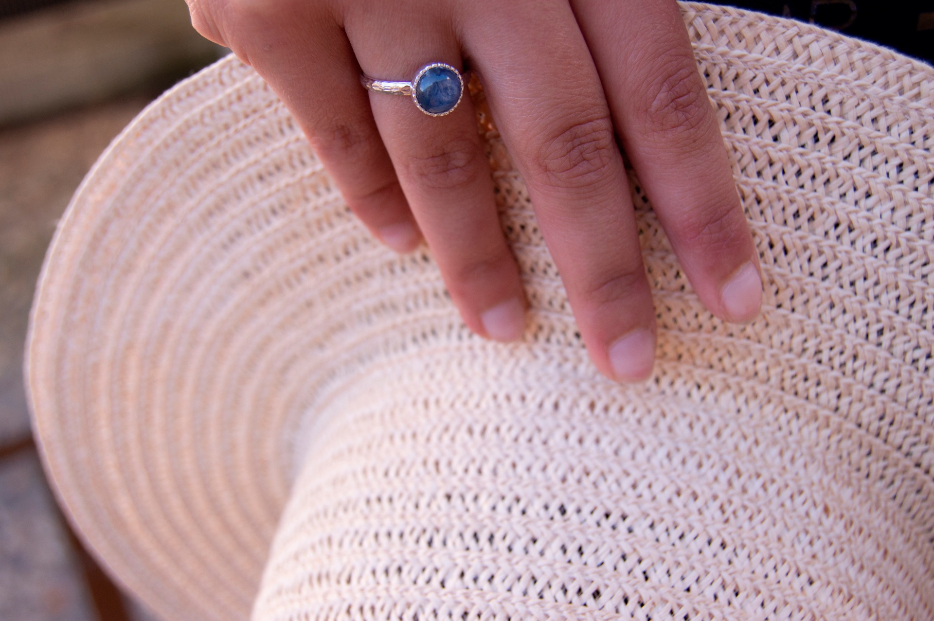 Anel com Pedra Natural Kyanit Mão com anel azul segurando chapéu de palha bege