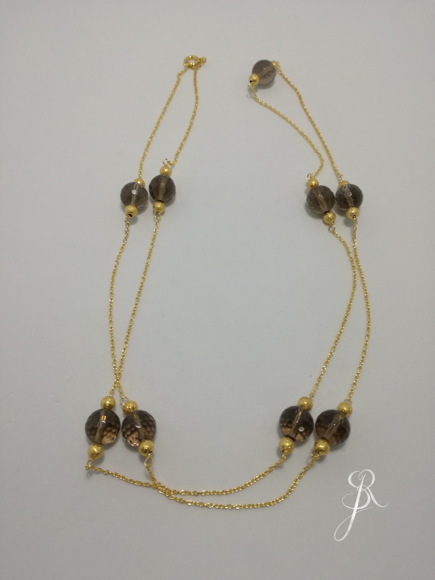 Colar Quartz Fume e Granitos Colar dourado com contas castanhas translúcidas sobre fundo branco