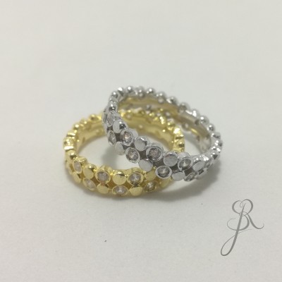 Dois anéis com cristais, um dourado e outro prateado, sobre fundo branco