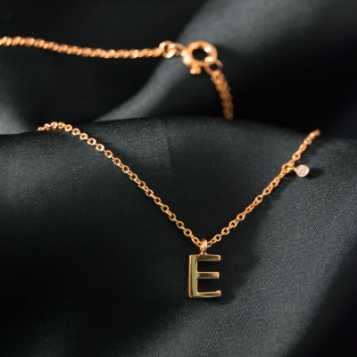 Colar dourado com pendente em forma da letra E e pequena pedra clara sobre tecido preto