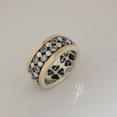Anel metálico prateado e dourado com padrão de círculos e manchas