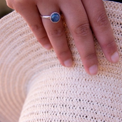 Mão com anel azul segurando chapéu de palha bege