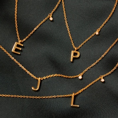 Colares dourados com letras E, P, J e L sobre tecido preto