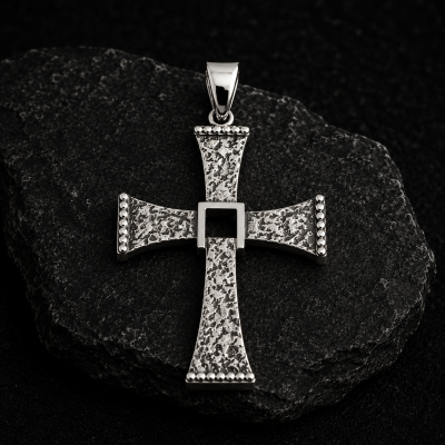Pendente em forma de cruz prateada com textura rugosa sobre pedra escura