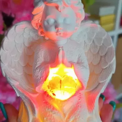 Figura decorativa de anjo branco a segurar luz amarela brilhante com fundo de flores cor-de-rosa