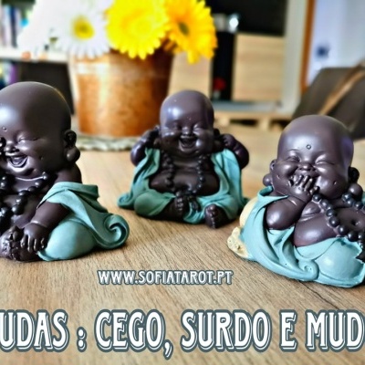 Três estatuetas de budas em madeira com roupas verdes, sobre mesa de madeira com vaso de flores ao fundo e texto promocional.