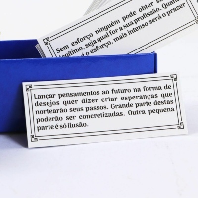 Cartões em papel branco com frases em português dentro de caixa azul sobre superfície branca
