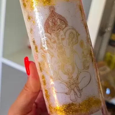 Vela branca decorada com glitter dourado e vermelho e desenho de Ganesha