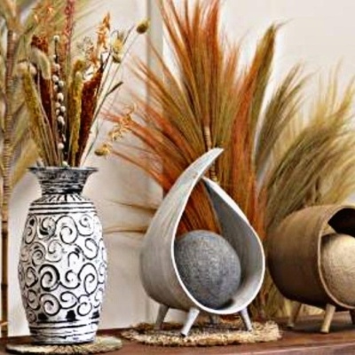 Três vasos decorativos com flores secas e folhagens em fundo claro