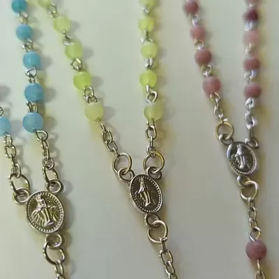 Três terços com contas coloridas azul, amarelo e rosa e medalhas religiosas ovais prateadas