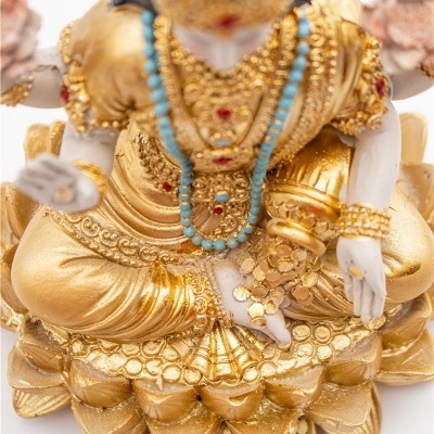 Estátua dourada de figura sentada com colares azuis e vermelhos sobre flor de lótus