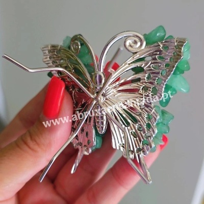 Presilha de cabelo borboleta metálica com pedras verdes, mão com unhas vermelhas