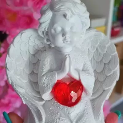 Estatueta anjo branco com coração vermelho translúcido em fundo floral cor-de-rosa