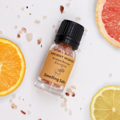 Frasco de sais aromáticos com rótulo amarelo e tampinha preta rodeado por frutas e cristais de sal