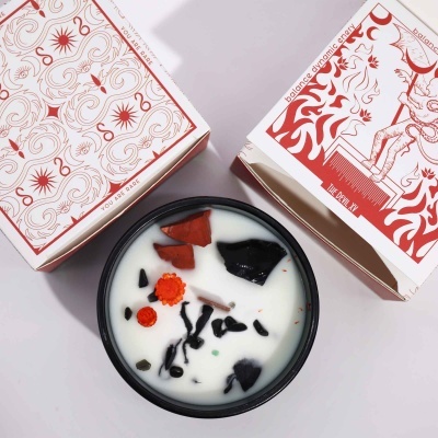 Vela aromática em copo preto com inclusões decorativas e embalagem branca com design vermelho