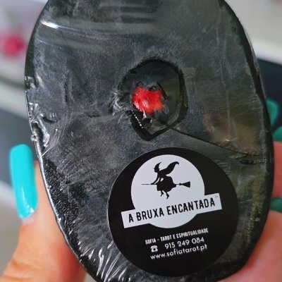 Produto preto irregular com etiqueta preta e branca de bruxa voando de vassoura e texto A BRUXA ENCANTADA