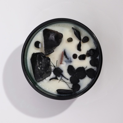 Vela aromática branca com inclusões negras num recipiente preto sobre fundo branco