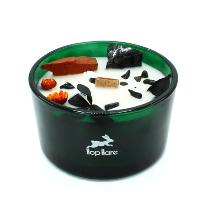 Vela aromática branca em recipiente verde escuro de vidro com decoração de pedras e elementos secos