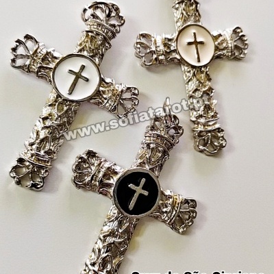 Três cruzes ornamentadas de metal prateado com círculos centrais contendo cruzes, duas brancas e uma preta.