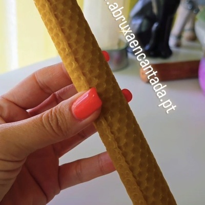 Vela de cera com padrão de favo de mel sendo segurada por uma mão