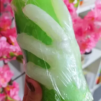 Vela verde e branca em forma de mão embrulhada em plástico