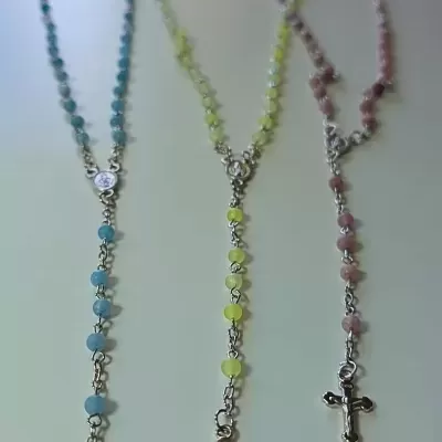 Três terços coloridos com crucifixos prateados sobre fundo branco