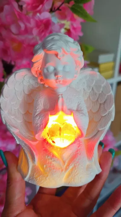 Figura decorativa de anjo branco a segurar luz amarela brilhante com fundo de flores cor-de-rosa