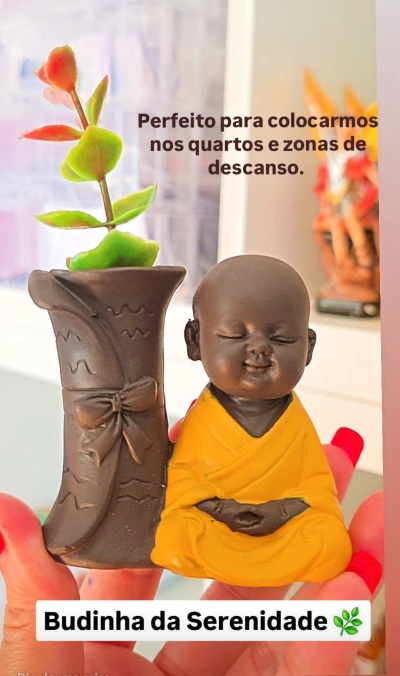 Estátua de buda sorridente ao lado de vaso decorativo com planta artificial.