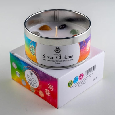 Vela aromática Seven Chakras em lata metálica com pedras coloridas em cima, sobre caixa colorida com símbolos.