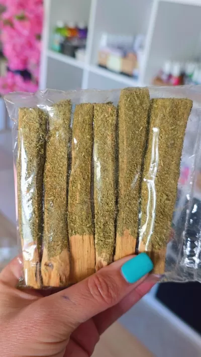 Palo santo embalado com ervas sendo segurado por mão com unha azul