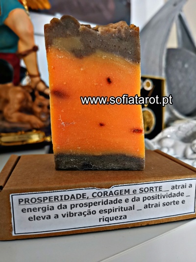 Sabonete artesanal com camadas coloridas e etiqueta com texto sobre prosperidade, coragem e sorte