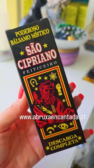 Embalagem preta com texto amarelo e vermelho de produto chamado São Cipriano, mão com unhas vermelhas segurando a caixa.