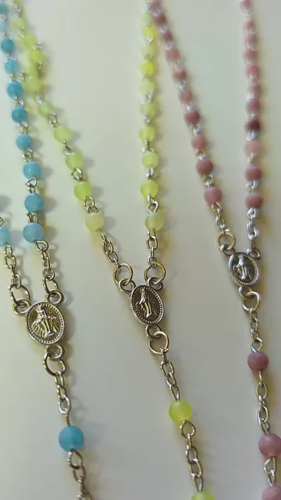 Três terços com contas coloridas azul, amarelo e rosa e medalhas religiosas ovais prateadas