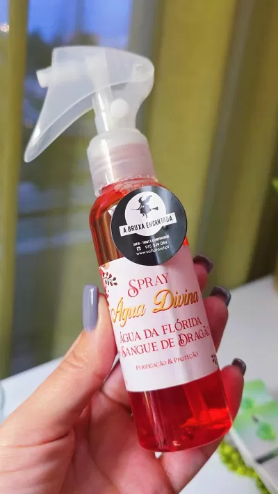 Frasco spray vermelho Água Divina com etiqueta A BRUXA ENCANTADA em fundo desfocado.