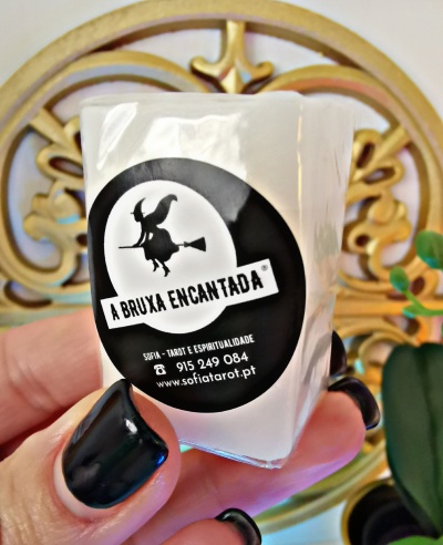 Embalagem com etiqueta preta de 'A BRUXA ENCANTADA', com texto e ilustração de bruxa, segura por mão com unhas pretas