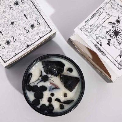 Velas aromáticas com cera branca e objetos pretos, caixas decoradas em fundo branco.