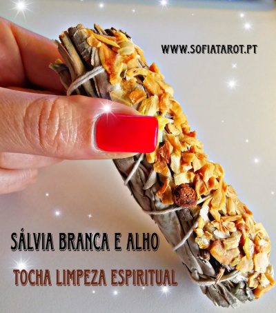 Tocha de limpeza espiritual com sálvia branca e alho sendo segurada por uma mão com unha vermelha, texto visível ao fundo.